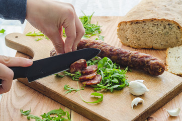 Woman's hands cutting sausage on a wooden kitchen board
