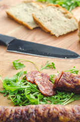 Domestic sausage, arugula, pieces of bread and a knife