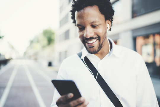 Closeup view of Attractive american african black man listening to music with headphones in urban background. Happy men using smartphone outdoors.Flares effects, blurred background.