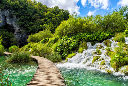 Tourist route on the wooden flooring in the famous Plitvice Lakes National Park across amazing colored water, green and waterfalls, nature background for guide book or poster