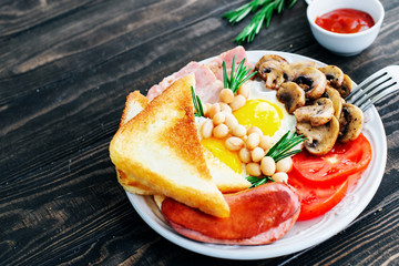 English breakfast eggs, bacon, beans, sausages, tomatoes, mushrooms decorated with rosemary and orange juice on a wooden table
