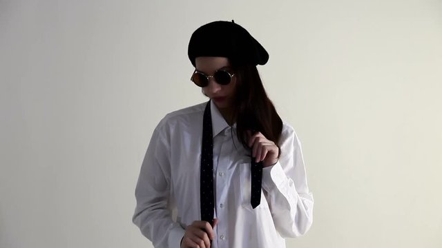 A Young woman in shirt, sunglasses and beret posing on the white background