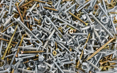 Steel and brass screws, nuts and metal dowels scattered on flat surface