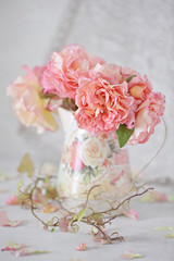 Beautiful garden roses in a jug on a table .