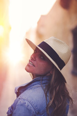 Young woman in hat looking back in sunset