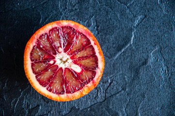 Whole and slices of fresh ripe blood oranges on a black slate background