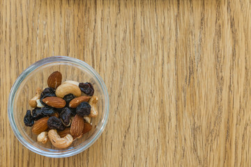 Breakfast when you are on a diet. Some nuts and raisins in a glass platter on a wooden table. Top view. Healthy food.