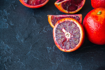 Whole and slices of fresh ripe blood oranges on a black slate background