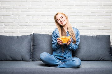 Young woman watching TV and eating chips on sofa at home