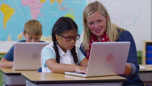 Teacher and young girl using laptop in classroom