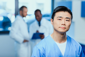 portrait of serious doctor in medical uniform with collegues behind in clinic