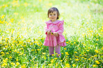 Girl in pink dress with dandelion on green grass.