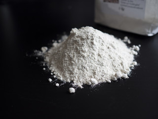 Wholemeal flour in a pile on black wooden table with a flour bag in the background