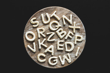 Top view of edible letters from dough on wooden cutting board, baking cookies concept