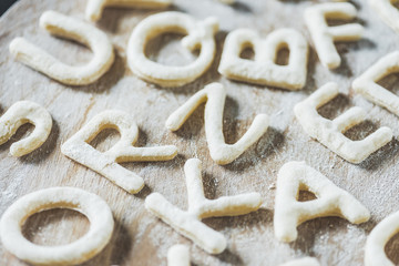 close up view of letters made from cookie dough on wooden board with flour