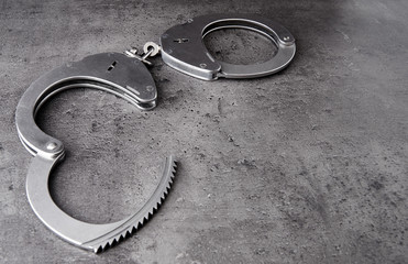 Opened police handcuffs on rough grey background with copy space.