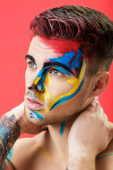 portrait of young man with colored face paint on red background. Professional Makeup Fashion. fantasy art makeup