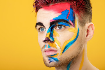 portrait of young man with colored face paint on yellow background. Professional Makeup Fashion. fantasy art makeup