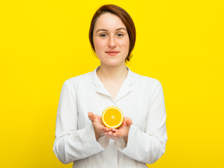 Young female nutritionist with half citrus on yellow background