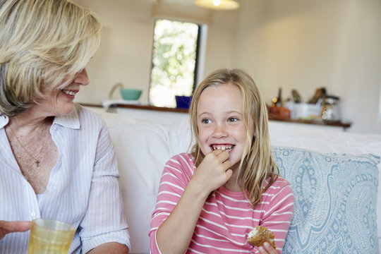 Portrait of smiling little girl eating sandwich while grandmother watching her