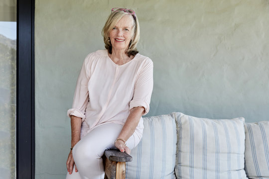 Portrait of smiling senior woman sitting on arm rest of a couch