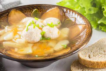 Meatball soup in a brown bowl with chives and bread.