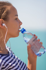 Sports girl drinks water during a workout on the beach. The girl drinks water during fitness outdoors