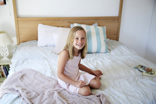 Portrait of smiling little girl sitting on bed at home