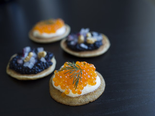 Homemade blinis with black and orange fish eggs, dill, onions and cream isolated on black background