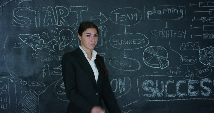 Beautiful business girl, marketing teacher, draws a graph of success on a black board, on a black background. Concept: career growth, growth chart, successful girl, marketing, ideas, finances.