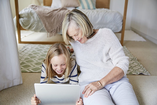 Little girl and her grandmother using tablet at home