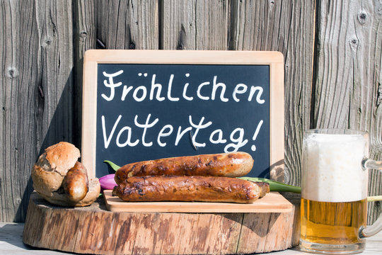 Tafel mit Text "Fröhlichen Vatertag" mit Bratwurst und Bier rustikal auf Holz