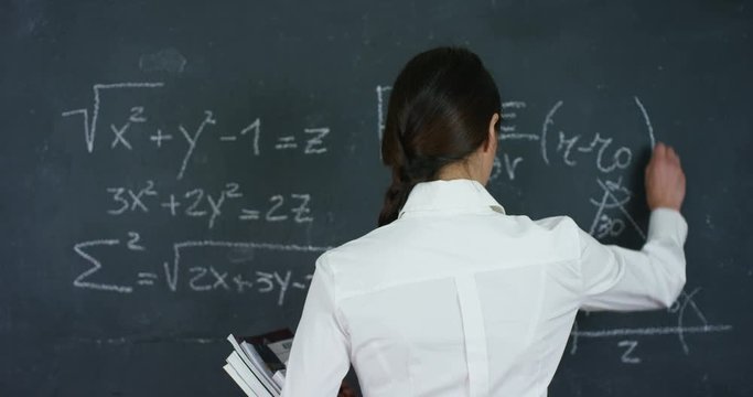 Portrait of a beautiful girl, teacher or student solves examples, formulas, triangle on a black board, on a black background. Concepts: ideas, algebra, mathematics geometry school university knowledge
