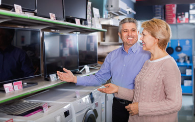 Fototapeta na wymiar Mature couple buy in shop of household appliances TV