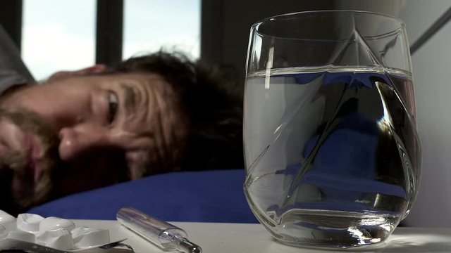 Sick man in bed measuring temperature focus on glass of water