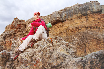 A girl traveler sits on a rock high in the mountains of the Caucasus against the backdrop of setting sun of rocks and sunset clouds