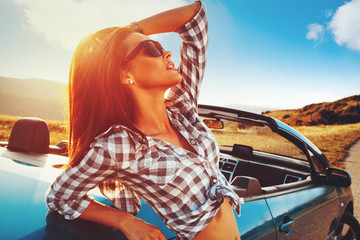 Attractive young woman with sunglasses posing leaning on convertible car during a sunny day