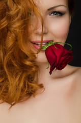 young woman with long red hair holds rose in her mouth
