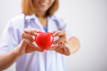 Female doctor holding a red heart shape with stethoscope. Health insurance and love concept.