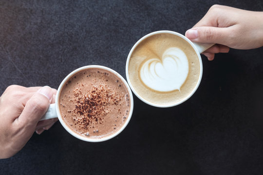 Top view image of man and woman's hands holding coffee and hot chocolate cups with wooden table background