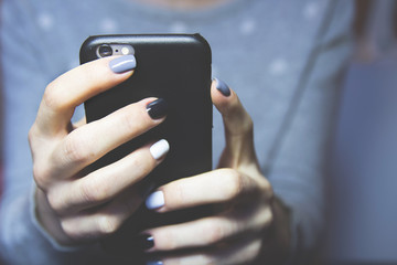Female hands with black, grey and white polished nails hold mobile phone
