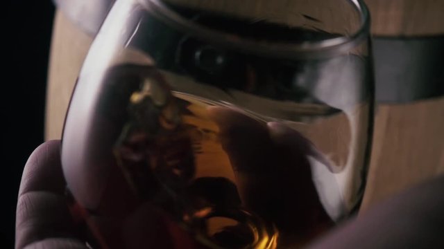 Slow mo. Cognac in a glass splashing in a man's hand against a barrel background