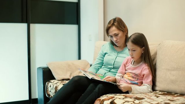 Mom and daughter reading a book sitting on the couch