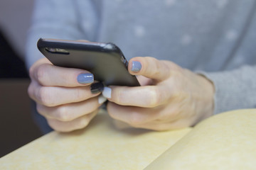 Female hands with black, grey and white polished nails hold mobile phone