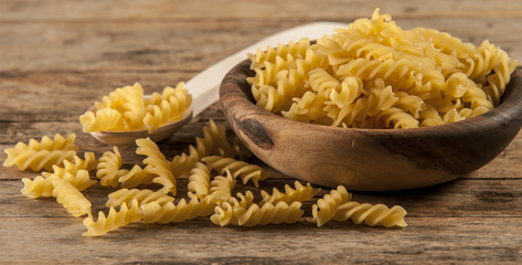 Pasta fusilli in a wooden bowl on wood background for healthy recipes.