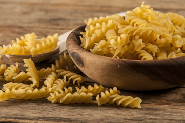 Pasta fusilli in a wooden bowl on wood background for healthy recipes.