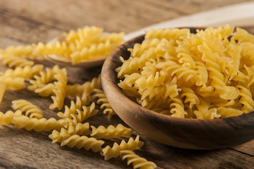 Pasta fusilli in a wooden bowl on wood background for healthy recipes.