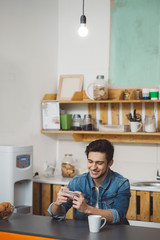 Young man sitting at a table in the kitchen with his mobile phone