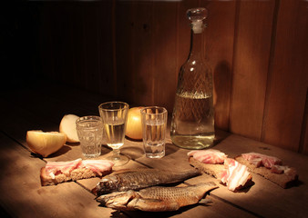 Still life with wine glasses and a decanter, fish, bread, onions and bacon on wooden boards