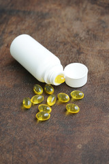 Fish oil capsule with pill bottle on wooden table. Health care and medical concept.